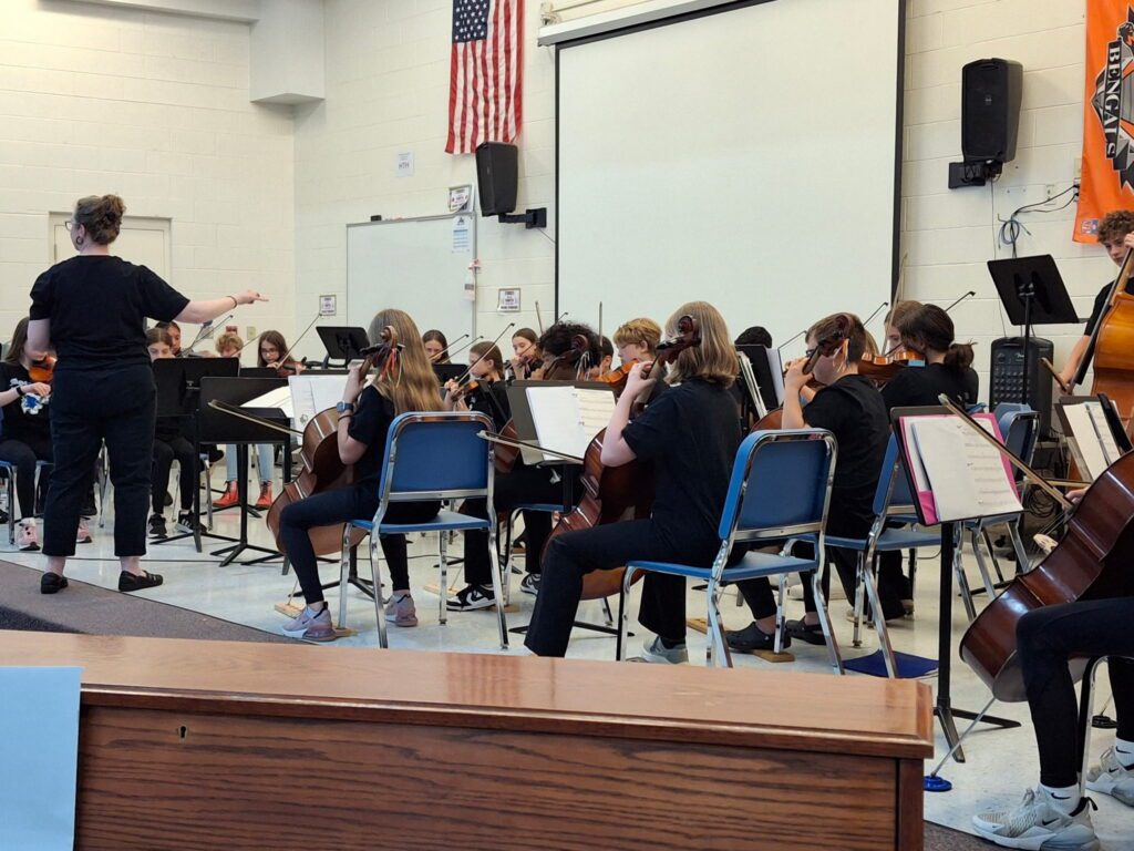 Miss Bartholic conducting a group of 6th grade Orchestra students on the gymnasium stage